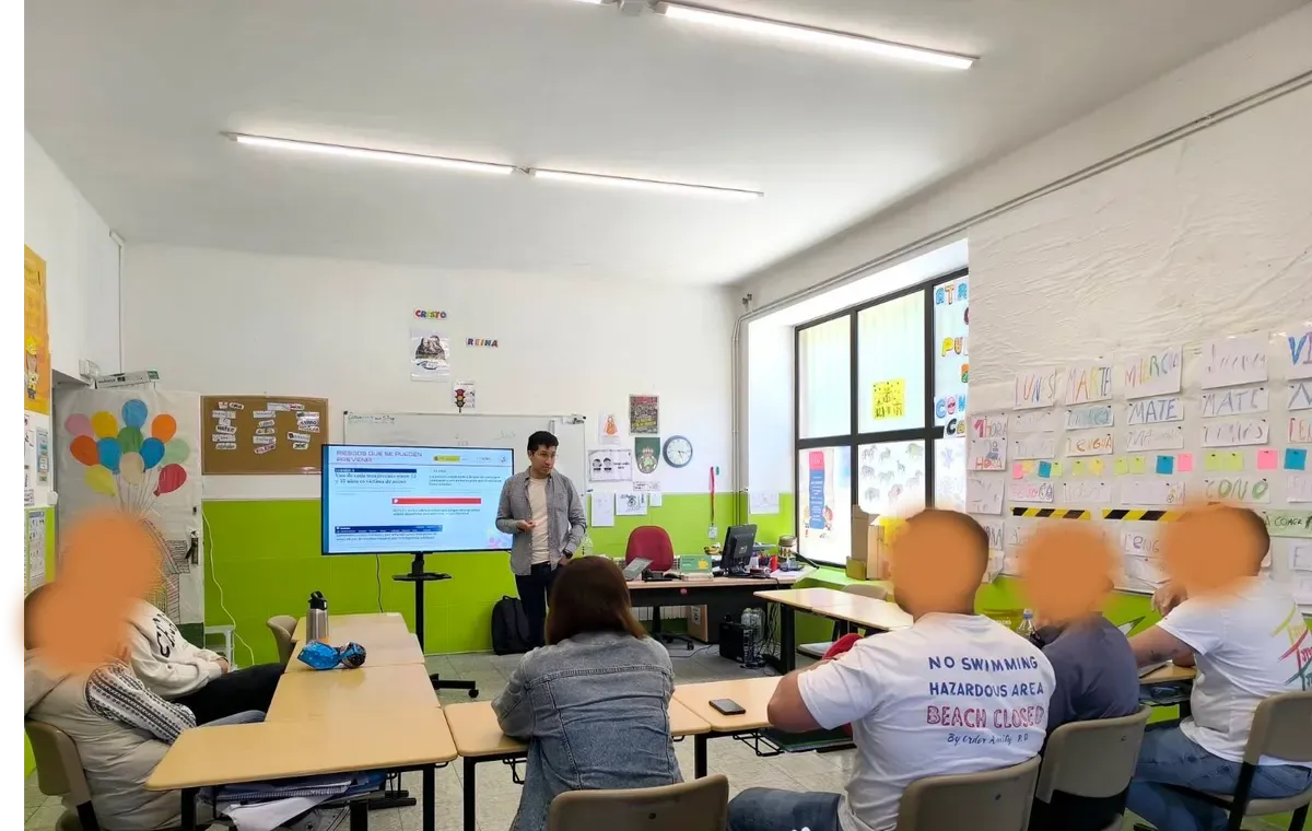 Bray Lozano in front of a screen showing the slide Riesgos que se pueden prevenir, at a workshop for adults seated at classroom tables